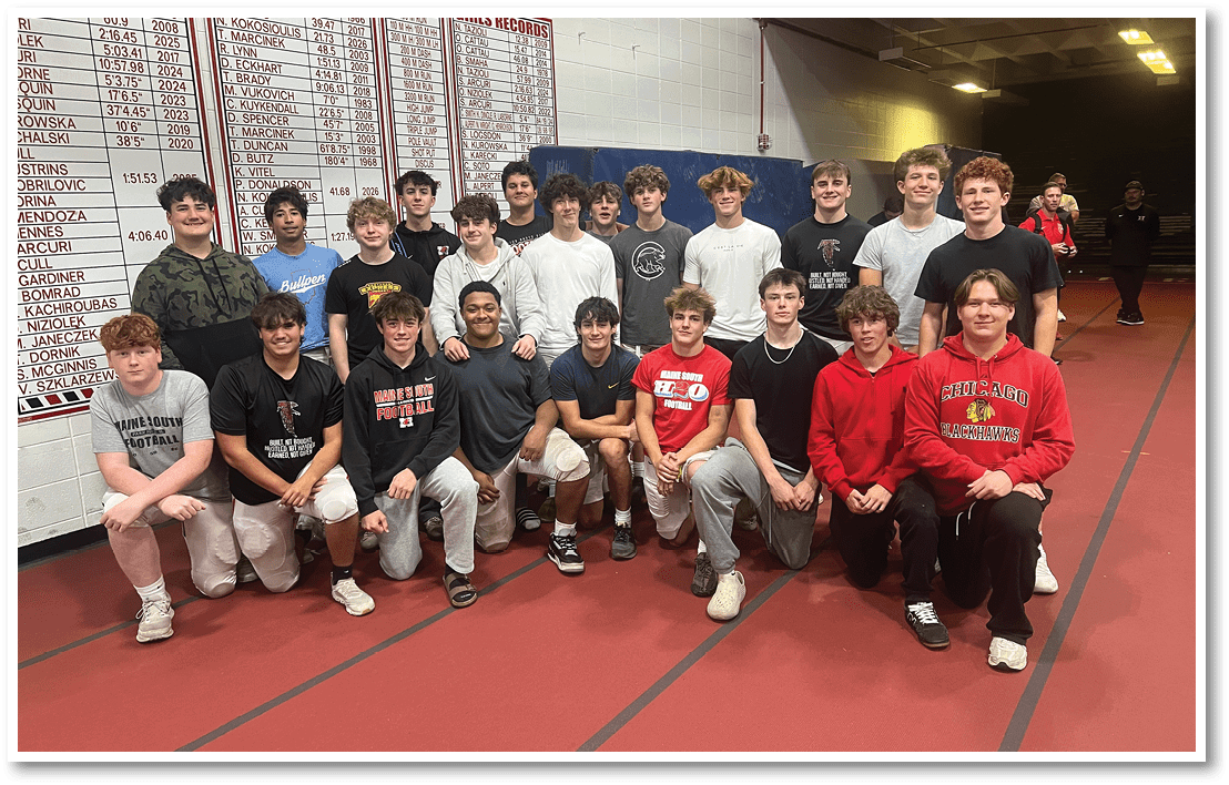 A group of people wearing casual and sports clothing pose together indoors in front of a wall with sports records and a blue mat. Description generated by AI