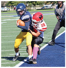 People wearing football uniforms are playing on a field with one person holding the ball while others are running and attempting to tackle. Description generated by AI