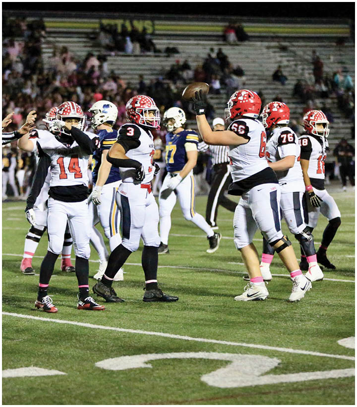 Several people in football uniforms are on a field with one person holding a football and others standing nearby during a game. Description generated by AI