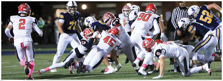 Several people in football uniforms are actively engaged in a play on a field during a nighttime game. Description generated by AI