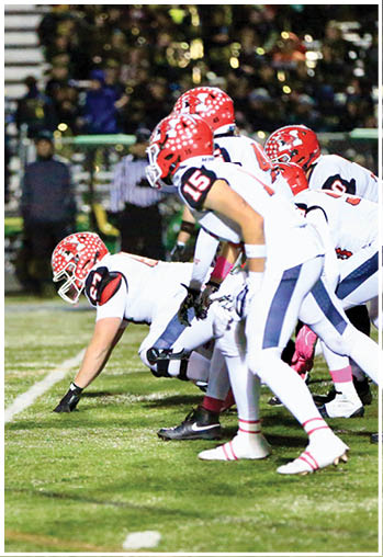 Two opposing American football teams in helmets and uniforms are lined up facing each other on a field, ready for the next play during a night game. Description generated by AI
