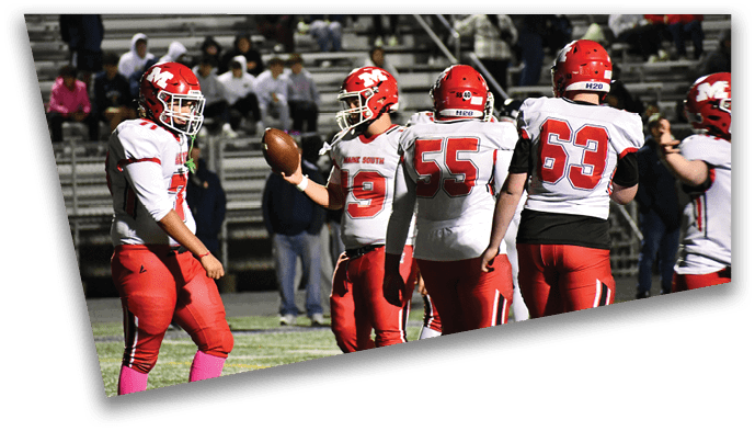 Four people wearing red and white football uniforms stand on a field with bleachers and spectators in the background. Description generated by AI