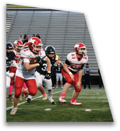Players in red and white uniforms are running on a football field with one player holding the ball while players in dark uniforms attempt to catch them. Description generated by AI