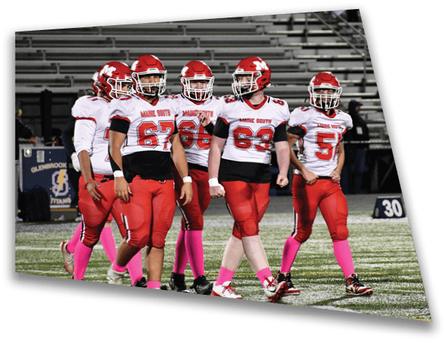 People wearing football uniforms with pink socks are standing on a field near a yard marker. Description generated by AI
