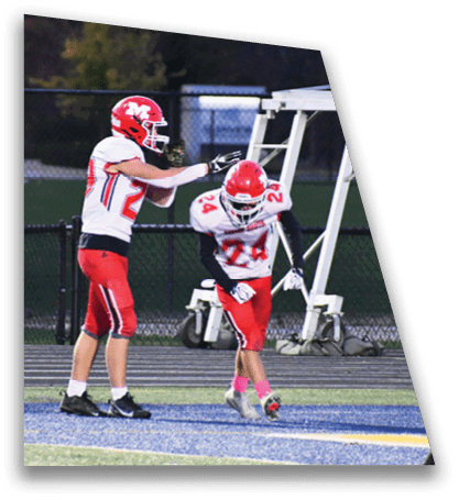 Two people in red and white football uniforms are on a field with one person reaching out to the other. Description generated by AI