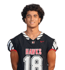 A person with curly hair is wearing a black sports jersey with the word “HAWKS" and the number 18 on the front, standing with hands behind their back and smiling. Description generated by AI