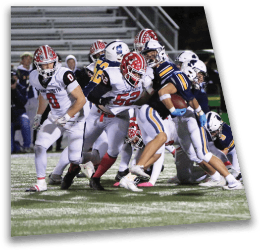 People in football uniforms are engaged in a close play on a field under stadium lights. Description generated by AI