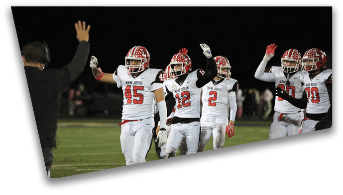People in football uniforms are raising their hands on a field at night while a person in dark clothing with a headset raises one hand toward them. Description generated by AI