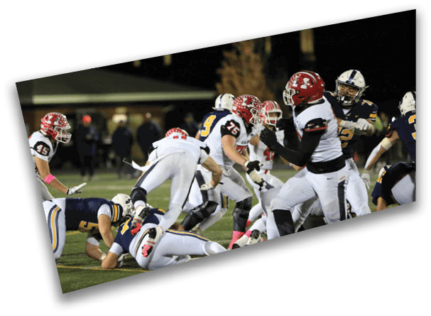 People wearing football uniforms are actively engaged in a play on a field during a nighttime game. Description generated by AI
