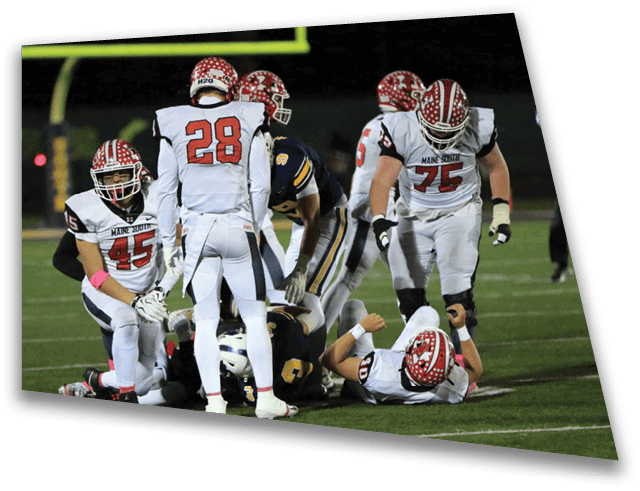 Several people in football uniforms are gathered on a field with one person lying on the ground and others standing or kneeling around them. Description generated by AI