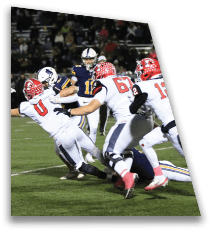 People in football uniforms are engaged in a tackle on a grassy field during a game. Description generated by AI