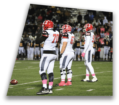 Three football players in white uniforms with red helmets and pink socks stand on a field near a football during a game with a crowd in the background. Description generated by AI