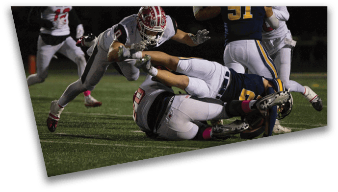 People in football uniforms are engaged in a tackle on a grassy field during a game. Description generated by AI