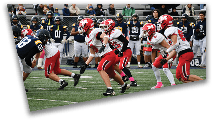 Players in red and white uniforms are running on a football field while players in dark uniforms are positioned to defend, with spectators watching from the bleachers in the background. Description generated by AI