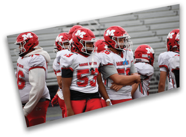 Several people wearing red and white football uniforms and helmets stand together on a field. Description generated by AI
