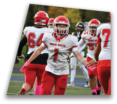 A person wearing a red and white football uniform with “Maine South" on the jersey is celebrating on a football field with teammates in the background. Description generated by AI