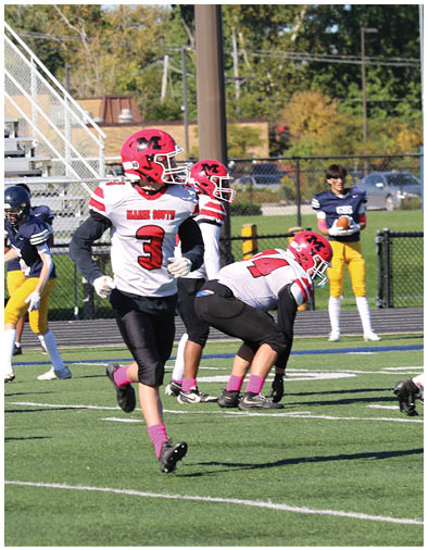 Three people in red and white football uniforms are on a green field with one person in a blue and yellow uniform holding a football in the background. Description generated by AI