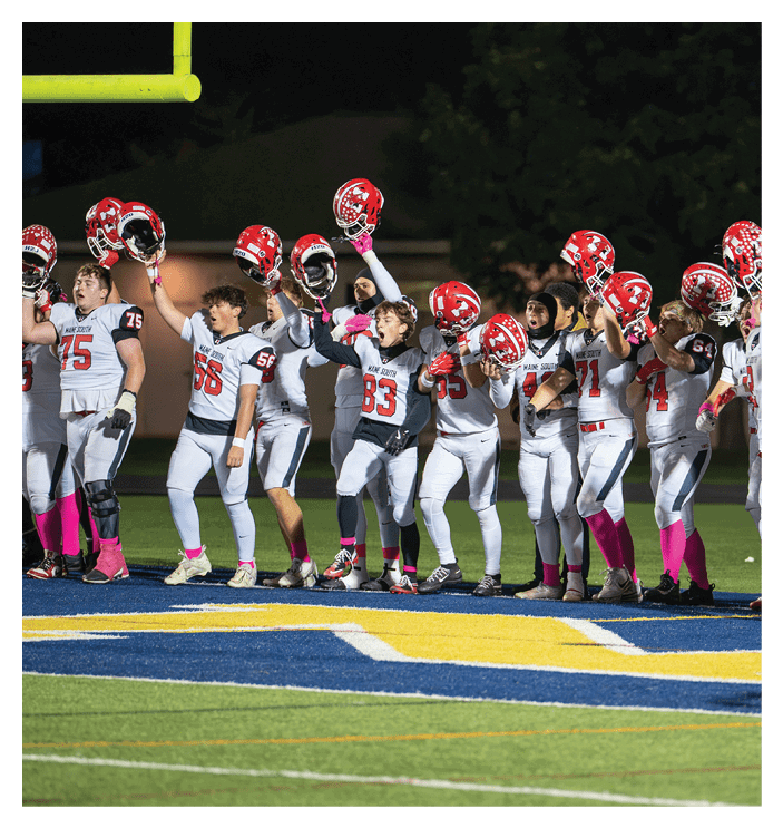 A group of people in football uniforms stand on a field holding red helmets up in the air, appearing to celebrate or acknowledge something. Description generated by AI