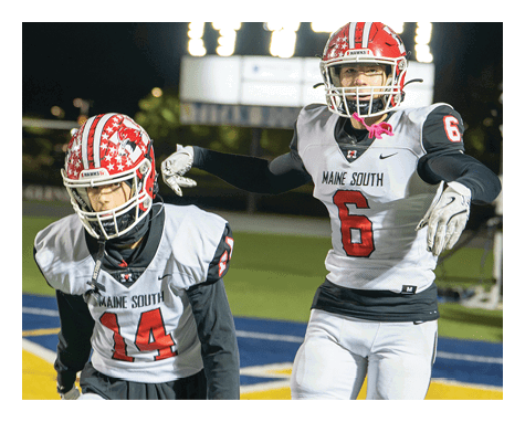 Two football players in helmets and uniforms are on the field with a scoreboard showing a tied score in the background at night. Description generated by AI
