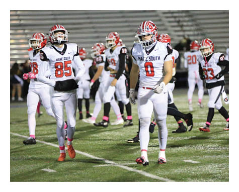 People in football uniforms are standing and walking on a grassy field during a game or practice. Description generated by AI