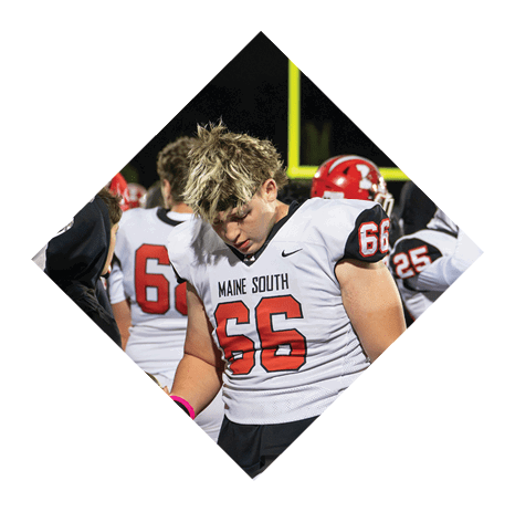 A person wearing a red football helmet with a white faceguard and a white jersey with the number 90 is sitting on a bench with other people in the background. Description generated by AI
