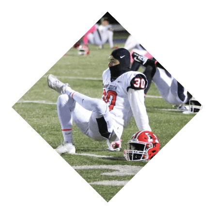 People in football uniforms are sitting and stretching on a field at night. Description generated by AI