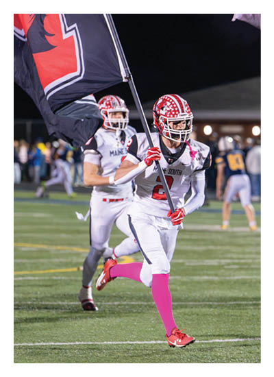 Two people in football uniforms are running on a field at night, with one holding a flag and wearing bright pink socks. Description generated by AI