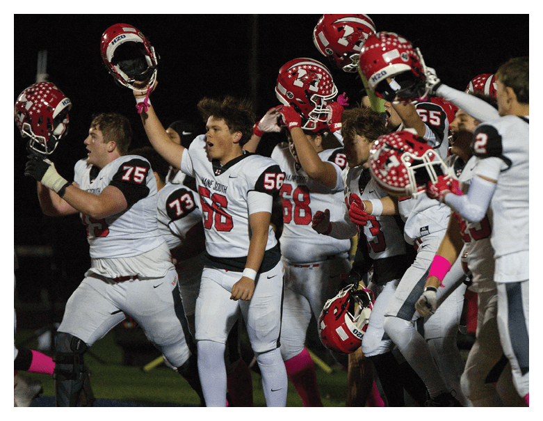 A group of football players in white uniforms with red helmets are celebrating energetically on a field at night. Description generated by AI