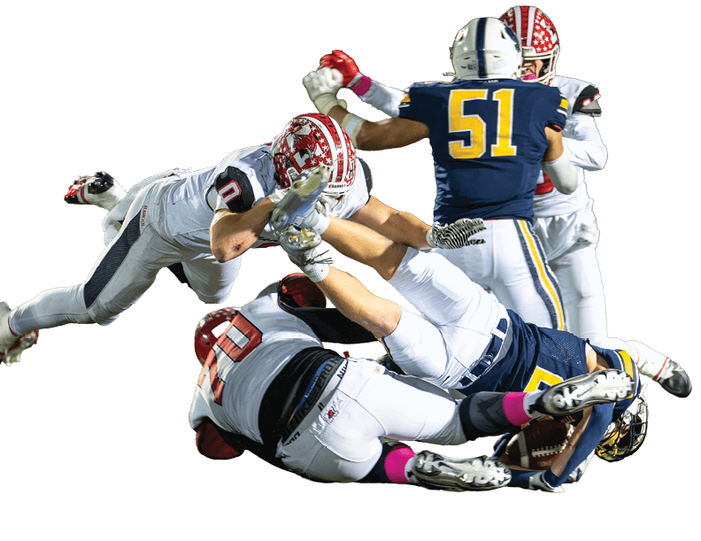 Several people in football uniforms are engaged in a dynamic play on a grassy field during a nighttime game. Description generated by AI