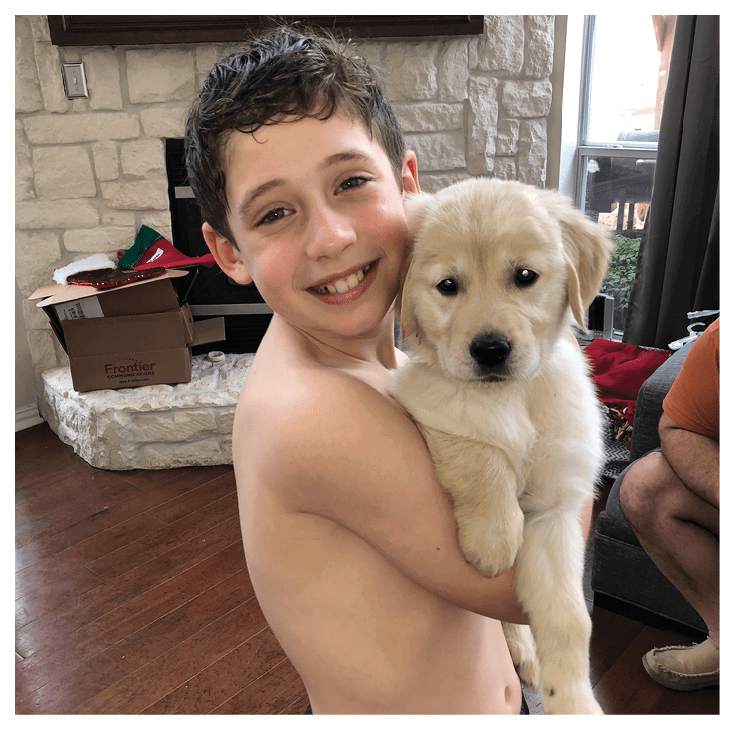 A person wearing a white shirt and blue jeans is sitting on a wooden bench in a park, holding a small dog on their lap. Description generated by AI