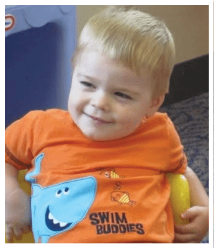A child with short light hair is smiling and wearing an orange shirt with a blue whale and fish design. Description generated by AI