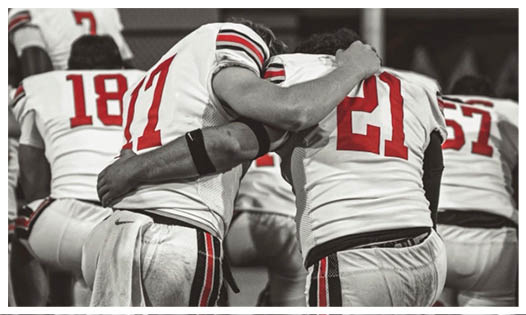 Two people wearing sports jerseys are embracing each other in a moment of consolation or support. Description generated by AI