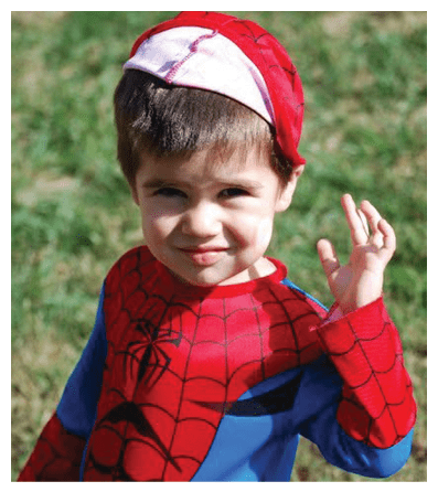 A child wearing a Spider-Man costume is standing outdoors on grass and waving with a slight smile. Description generated by AI