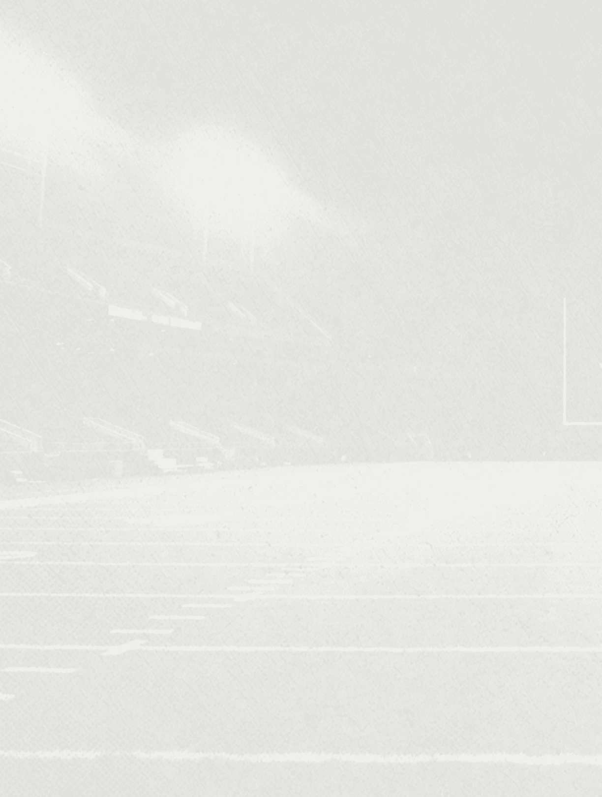 A foggy or snowy outdoor sports field with faint outlines of goalposts and stadium seating in the background. Description generated by AI