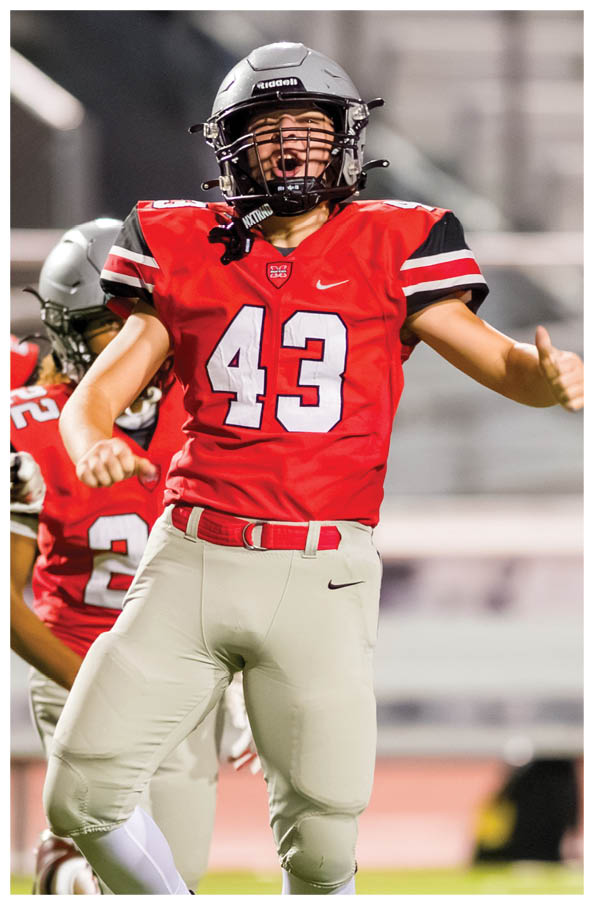 People in red and white football uniforms are celebrating on a field with one person in the foreground showing excitement with arms raised. Description generated by AI