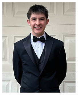 A person dressed in a formal black tuxedo with a bow tie stands in front of a white garage door. Description generated by AI