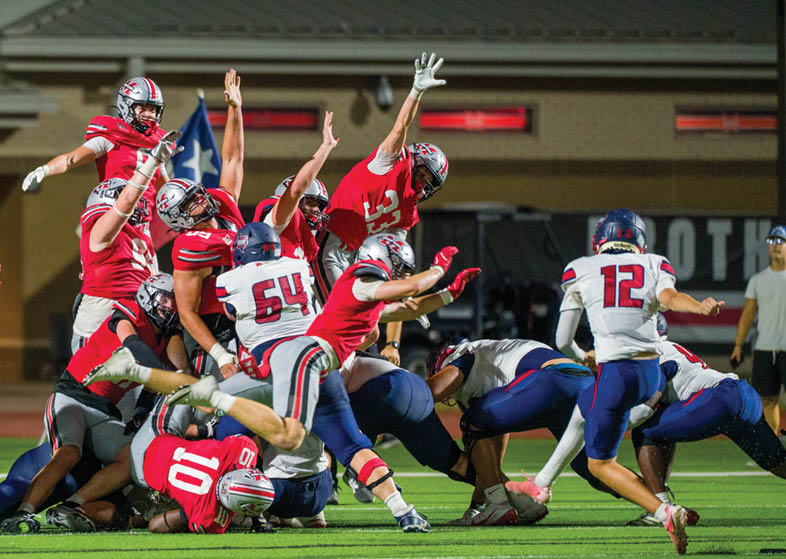 A group of people wearing football uniforms are actively engaged in a play on a well-lit field during a nighttime game. Description generated by AI