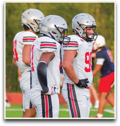 Three football players are standing on the field, one of them is smiling and wearing a black jersey with the number 55. AI generated content