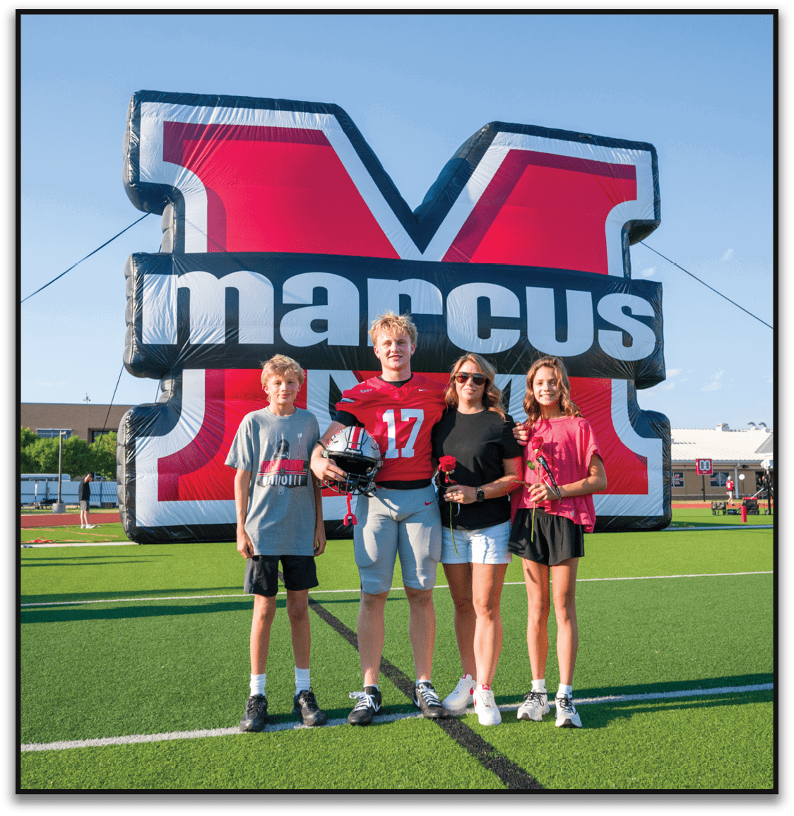 Three people smiling and posing in front of a large inflatable structure with bold red, white, and black colors and partially visible text. Description generated by AI