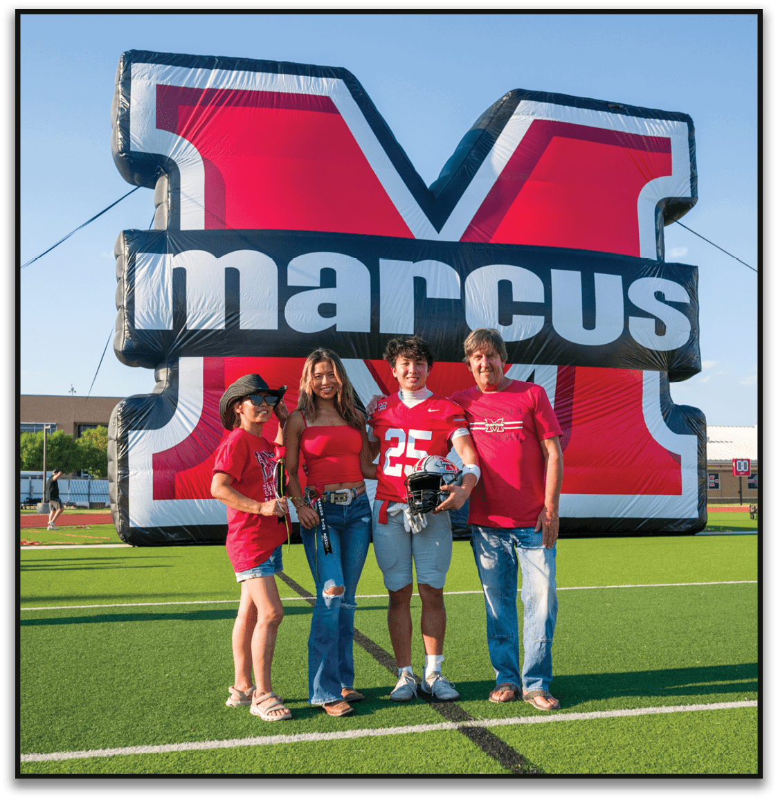 Three people smiling and standing in front of a large inflatable backdrop with bold red, black, and white colors and partially visible text. Description generated by AI