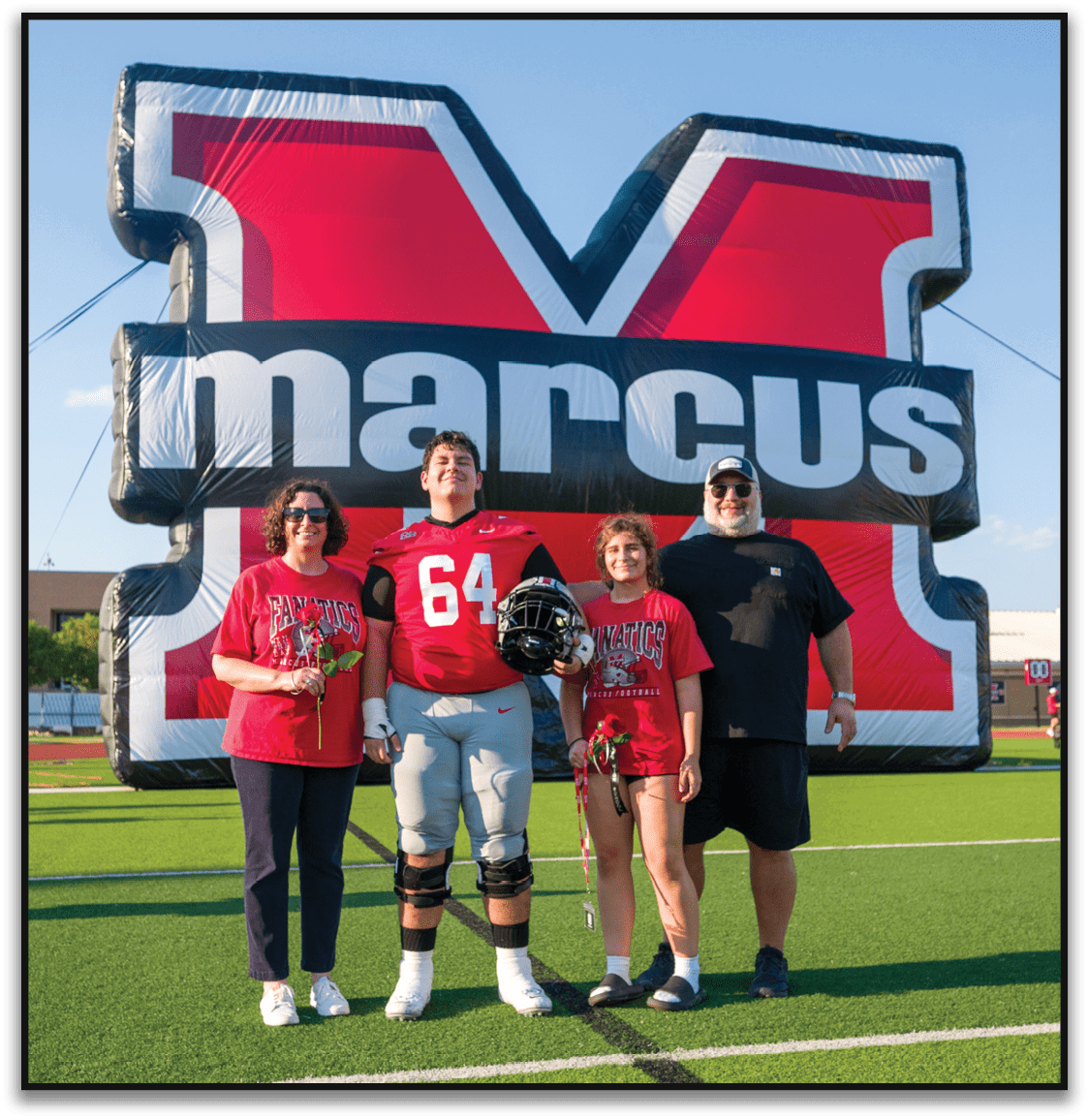 Three people stand smiling in front of a large red and black inflatable structure with partial white text, one wearing a red sports jersey with the number 64 and holding a helmet. Description generated by AI
