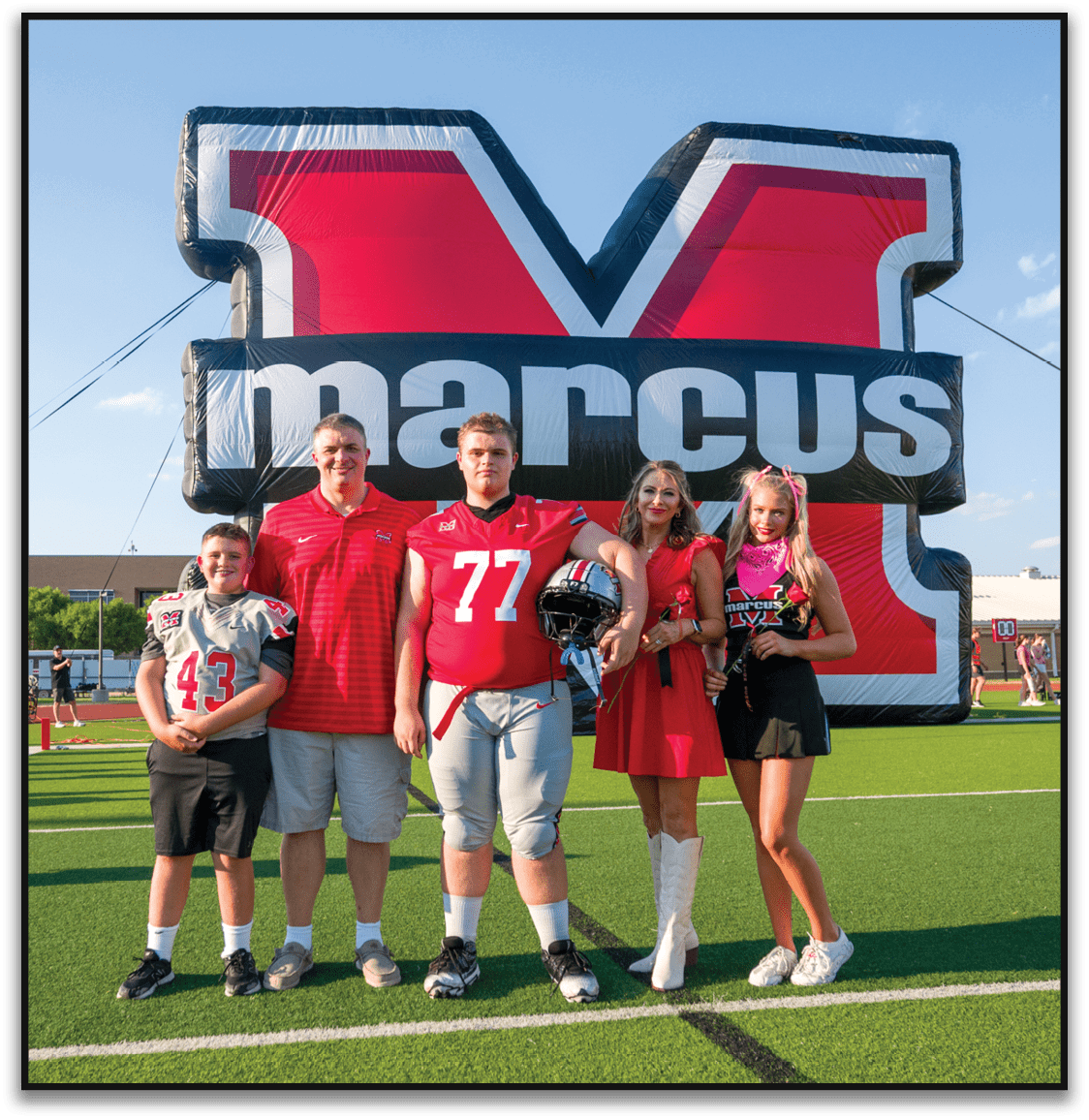 Three people wearing sports attire pose in front of a large inflatable sign with the word “marcus" on it, with one person holding a football helmet. Description generated by AI
