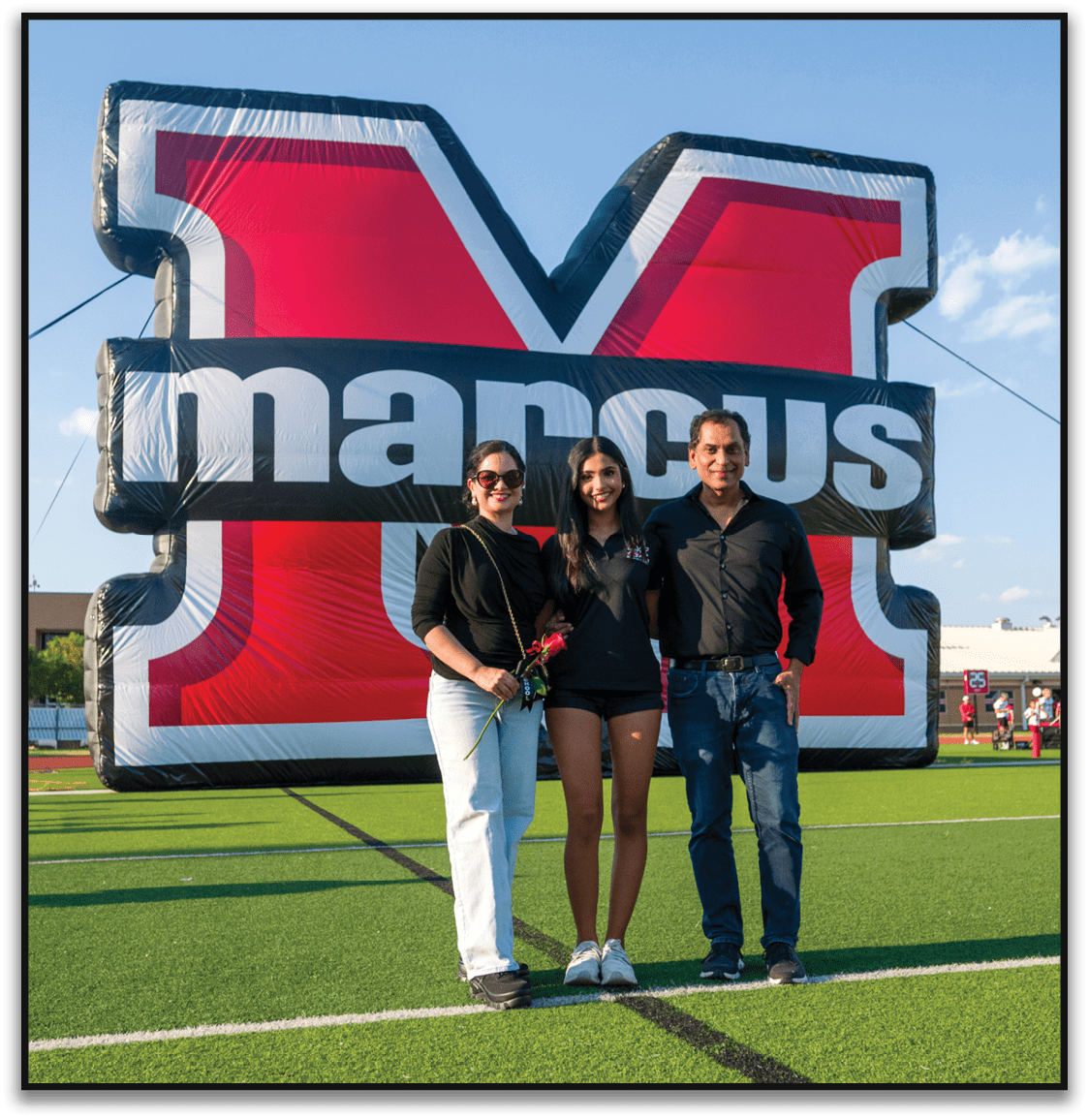 Three people smiling and standing close together in front of a large inflatable sign with bold red, white, and black colors. Description generated by AI