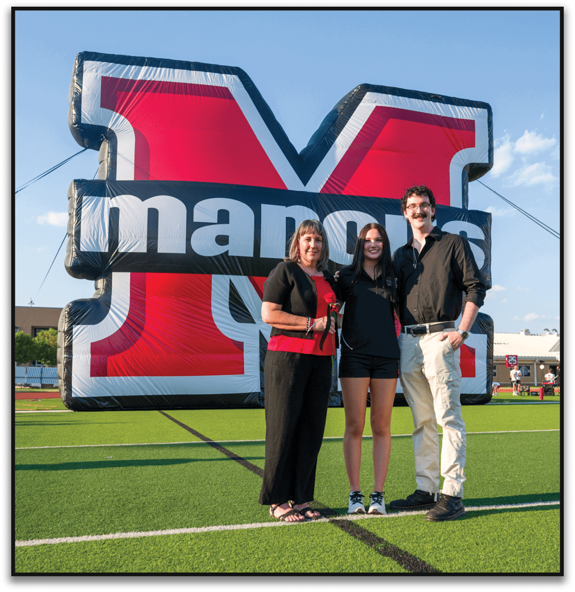 Three adults standing closely together smiling in front of a large inflatable structure with bold red, white, and black colors outdoors under a clear sky. Description generated by AI