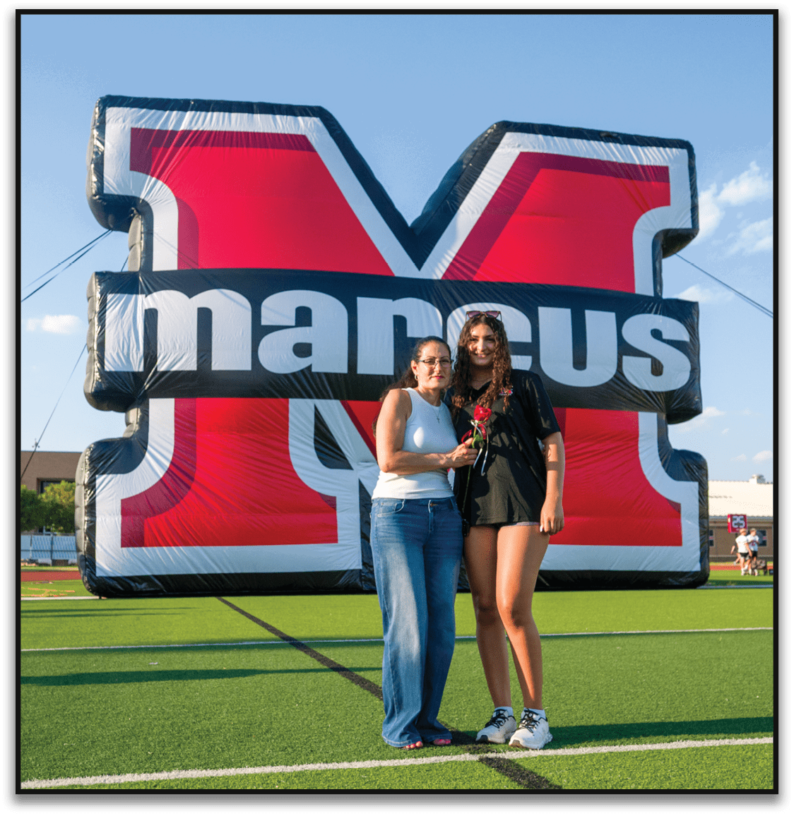Two people stand closely together smiling in front of a large red and black inflatable structure with white text. Description generated by AI