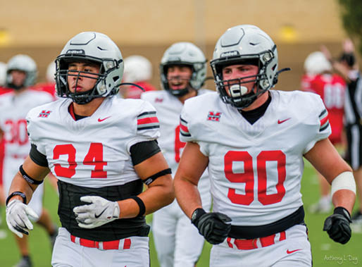 Three football players are standing on the field, one of them is smiling and wearing a black jersey with the number 55. AI generated content