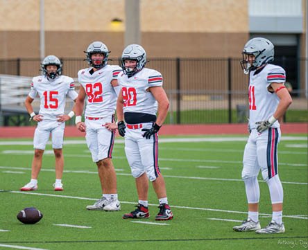 Three football players are standing on the field, one of them is smiling and wearing a black jersey with the number 55. AI generated content
