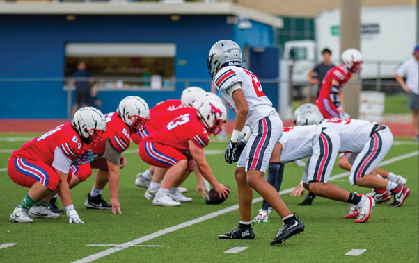 Three football players are standing on the field, one of them is smiling and wearing a black jersey with the number 55. AI generated content