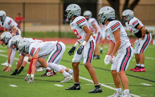 Three football players are standing on the field, one of them is smiling and wearing a black jersey with the number 55. AI generated content