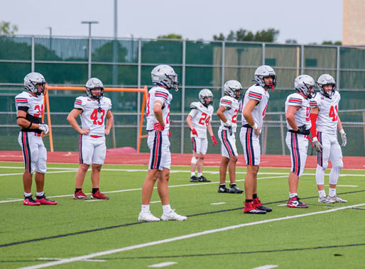 Three football players are standing on the field, one of them is smiling and wearing a black jersey with the number 55. AI generated content